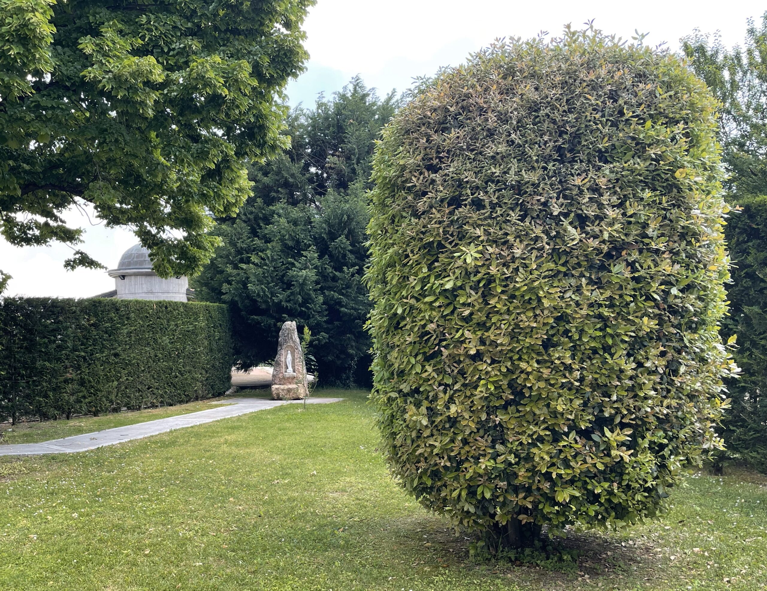 Siepi potate, vialetto in pietra e monumento decorativo in un’area verde tranquilla